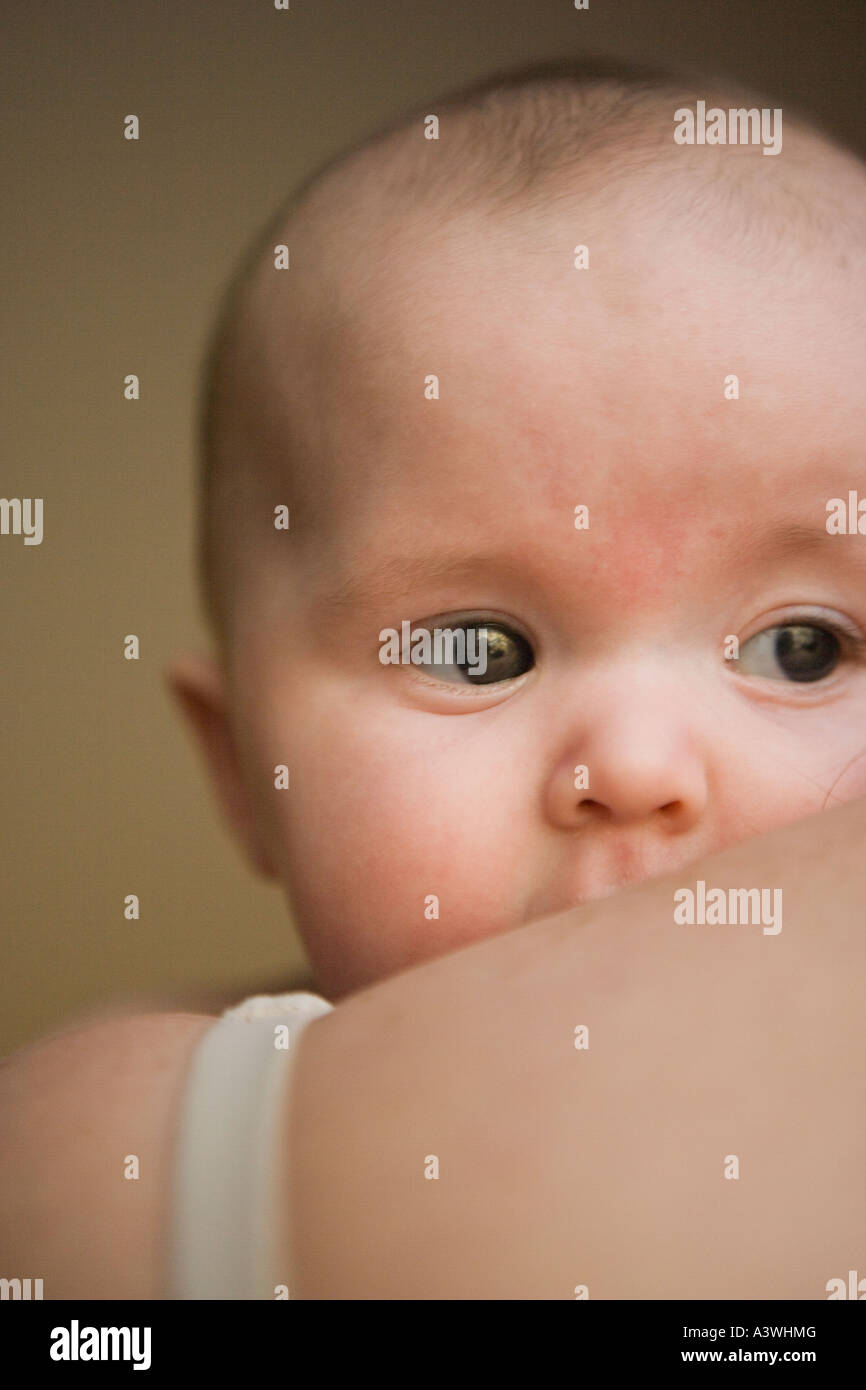 three to four month old baby girl peeking over mother's shoulder Stock Photo
