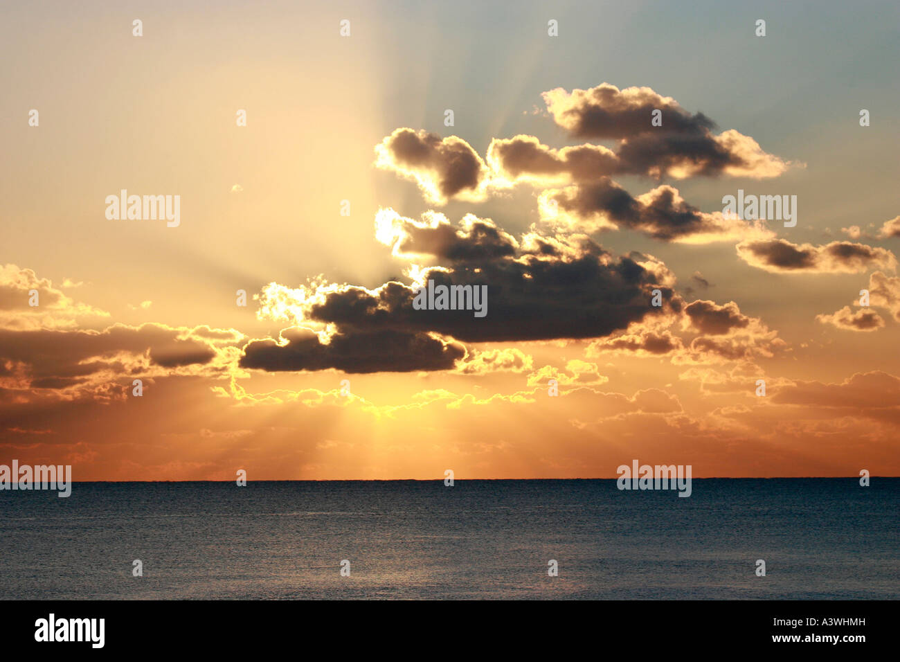 sunset through clouds over a silver sea Stock Photo