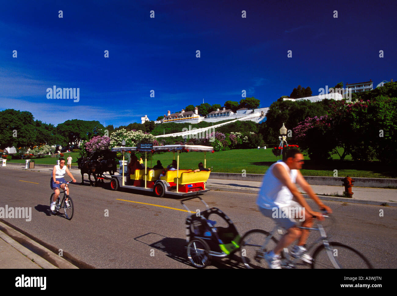 BICYCLISTS AND HORSE DRAWN CARRIAGES TRAVEL THE STREETS OF MACKINAC ISLAND MICHIGAN BELOW FORT MACKINAC Stock Photo