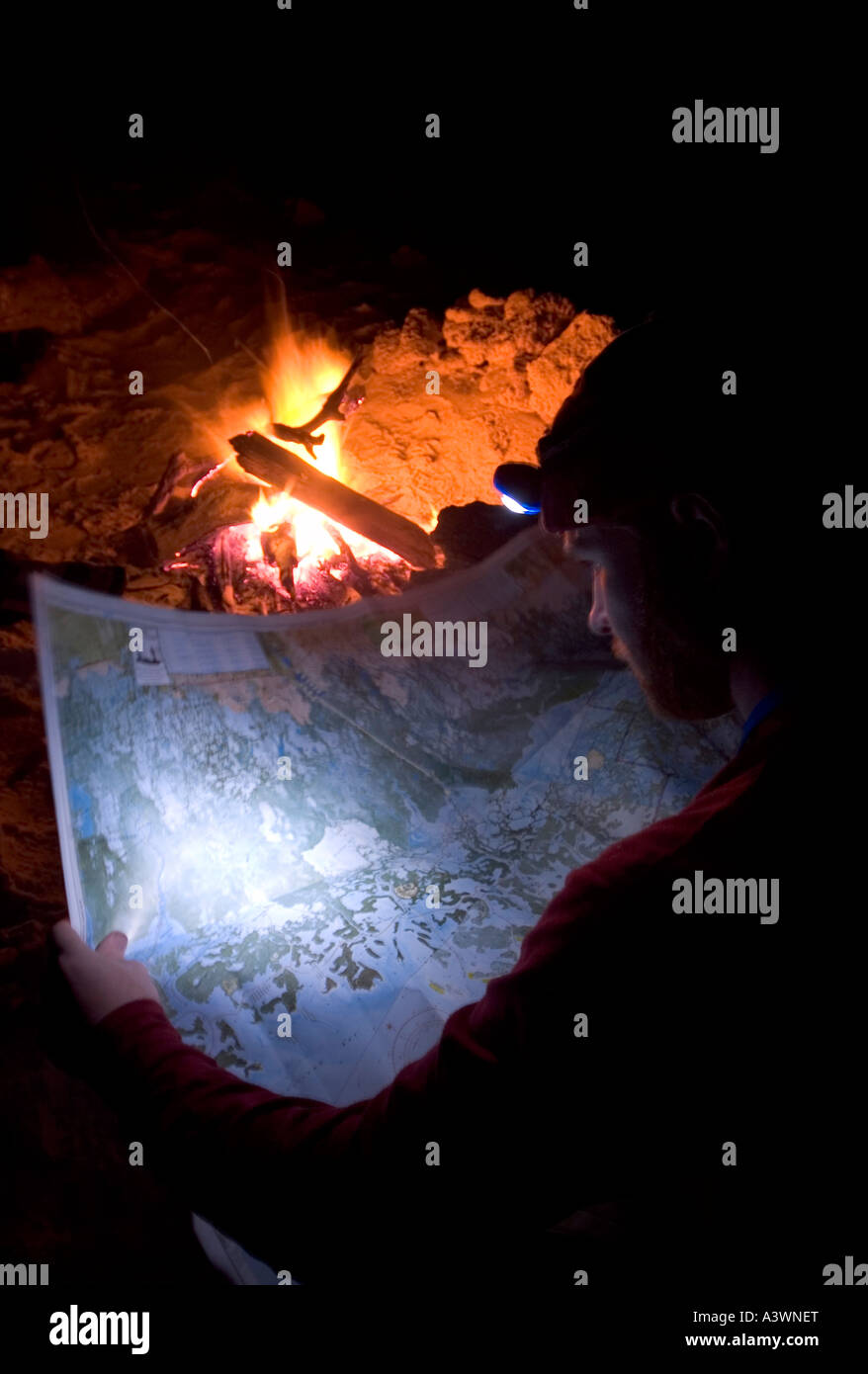 A backcountry camper looks over a nautical chart by a campfire on Round Key in the Everglades of South Florida Stock Photo