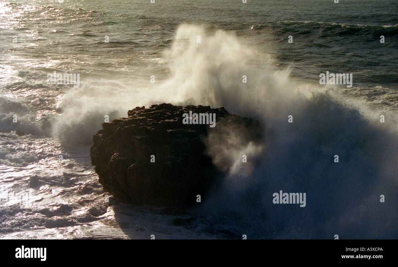 Sunlight highlighting a wave crashing over a rock Stock Photo - Alamy