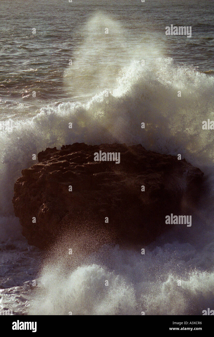 Wave caught in sunlight crashing into a rock Stock Photo - Alamy
