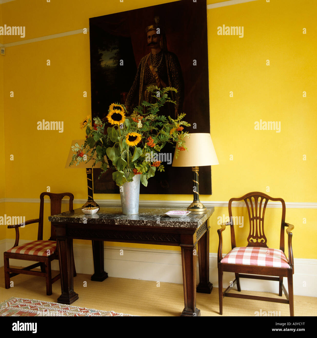 Sunflowers on console table with two chairs under artwork on yellow