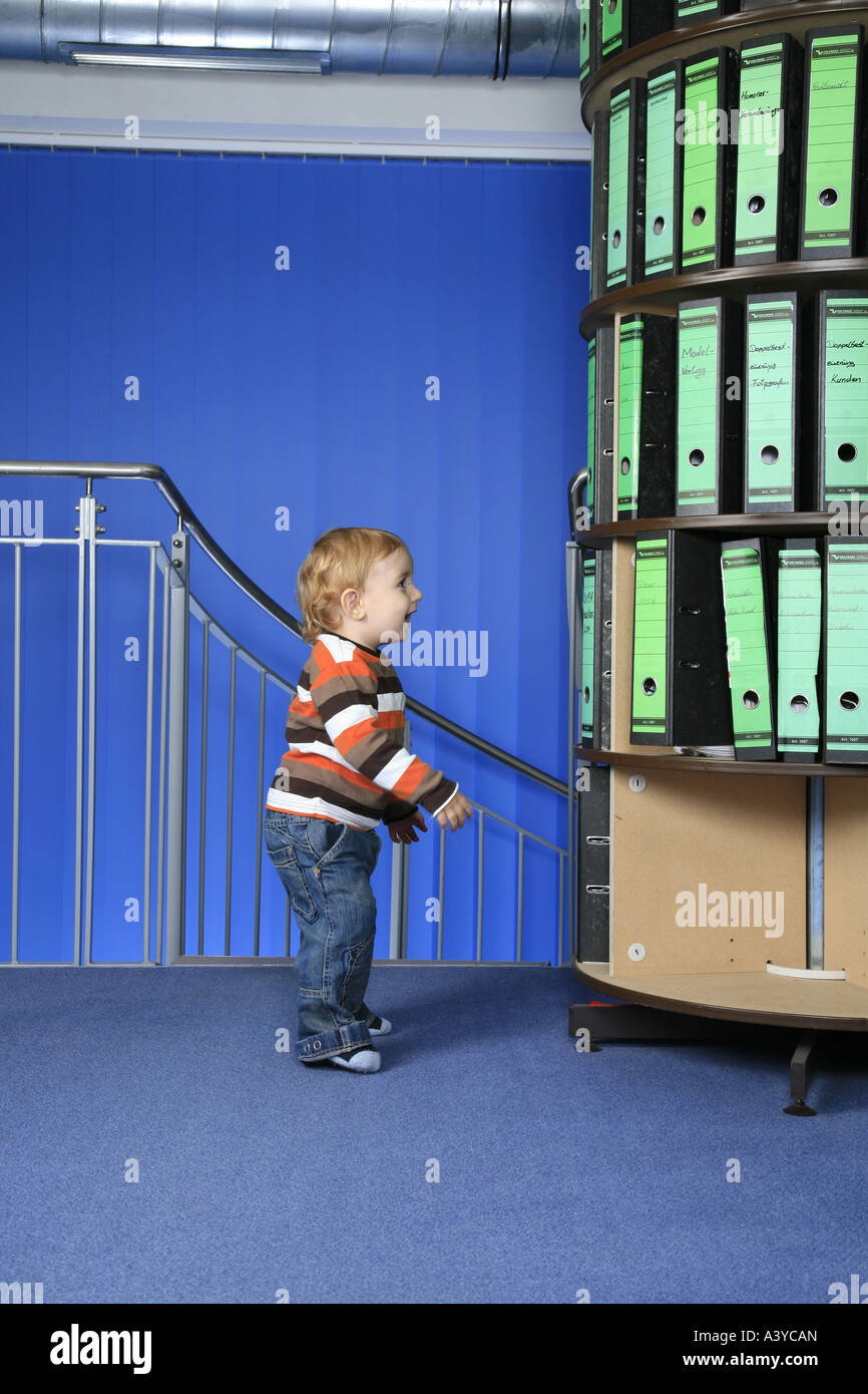 small laughing boy in front of a folder storage rack in the office ...