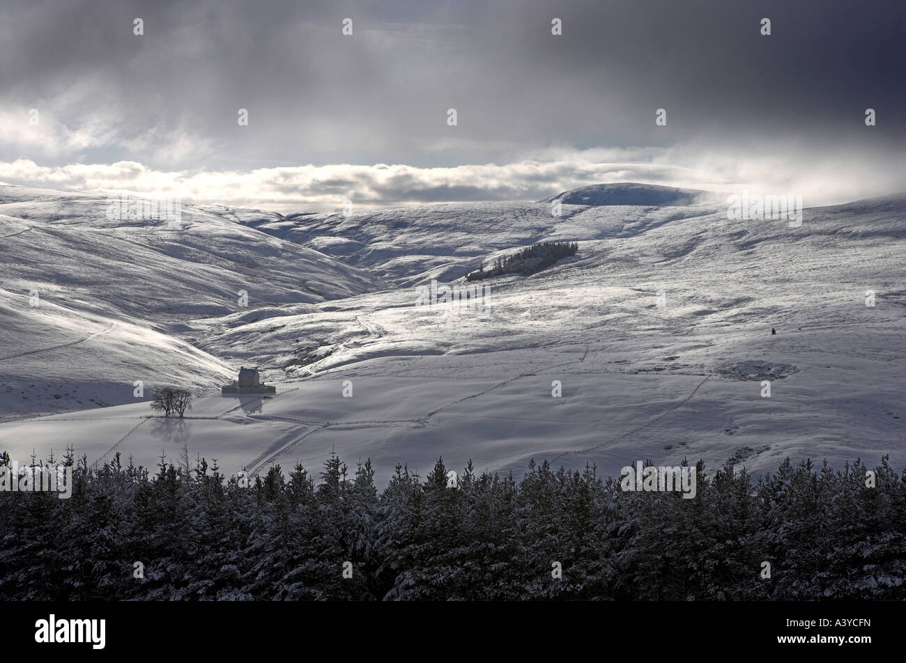 Landscape format image of Corgarff Castle, Scotland in Winter with Snow and moody skies shining on the dramatic mountainscape Stock Photo