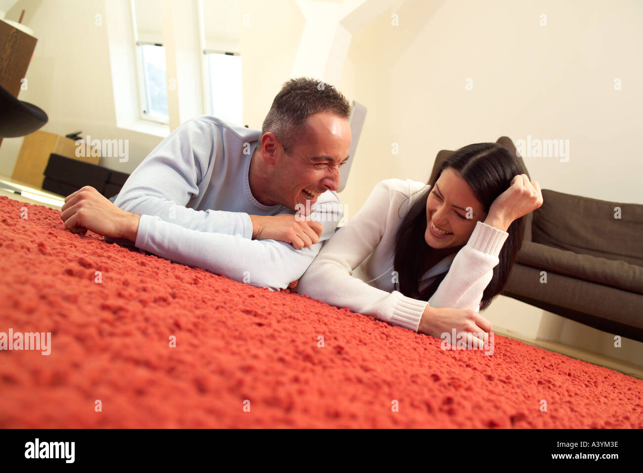 young couple lying on the carpet having a laugh Stock Photo