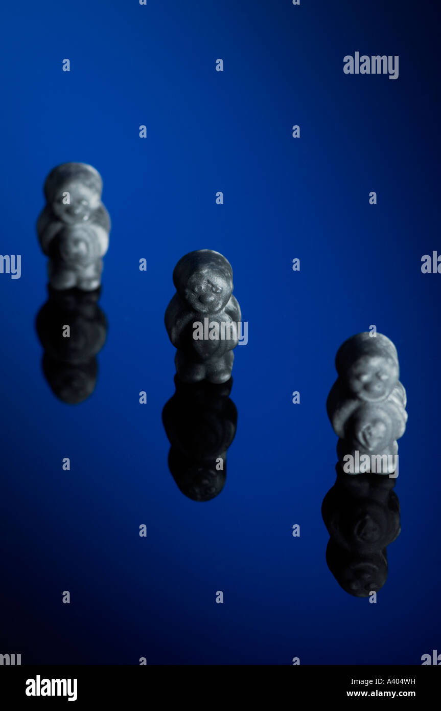 Three black jelly babies standing on a blue background. Stock Photo