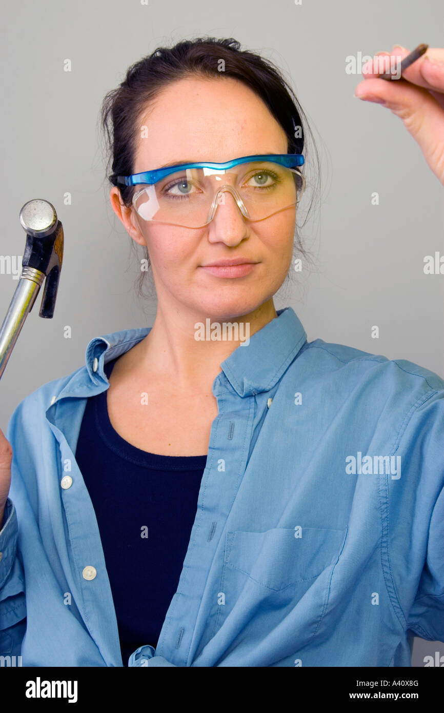 Young woman wearing safety glasses driving in nail as part of diy
