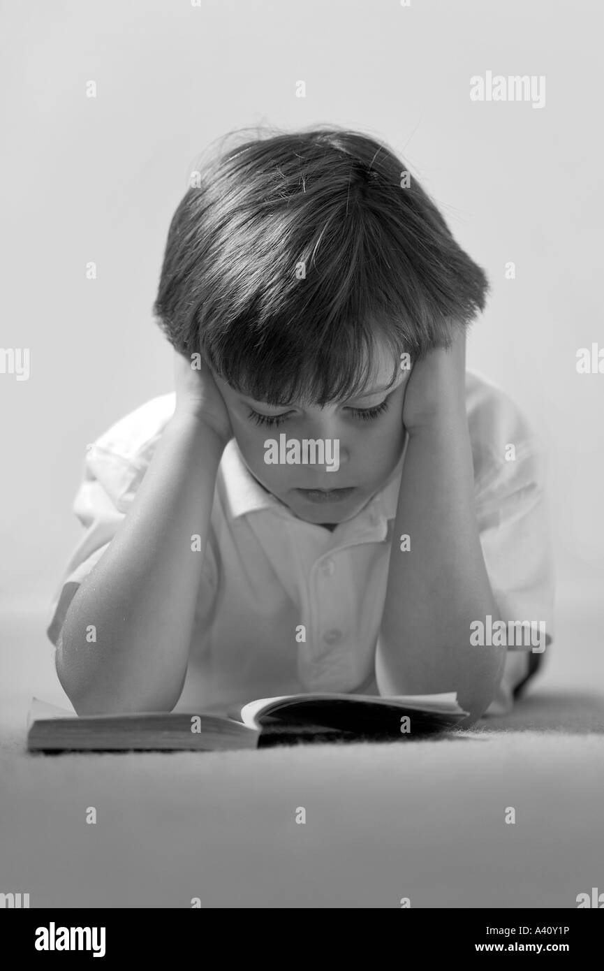 A Black White image of a boy reading a book with his head in his hands Stock Photo