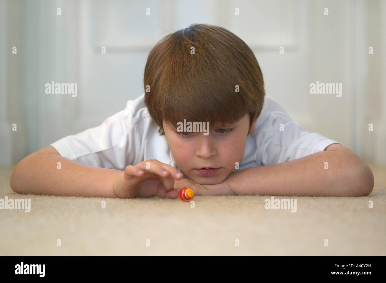 Young boy lying down about to flick a marble a look of concentration on his face Stock Photo