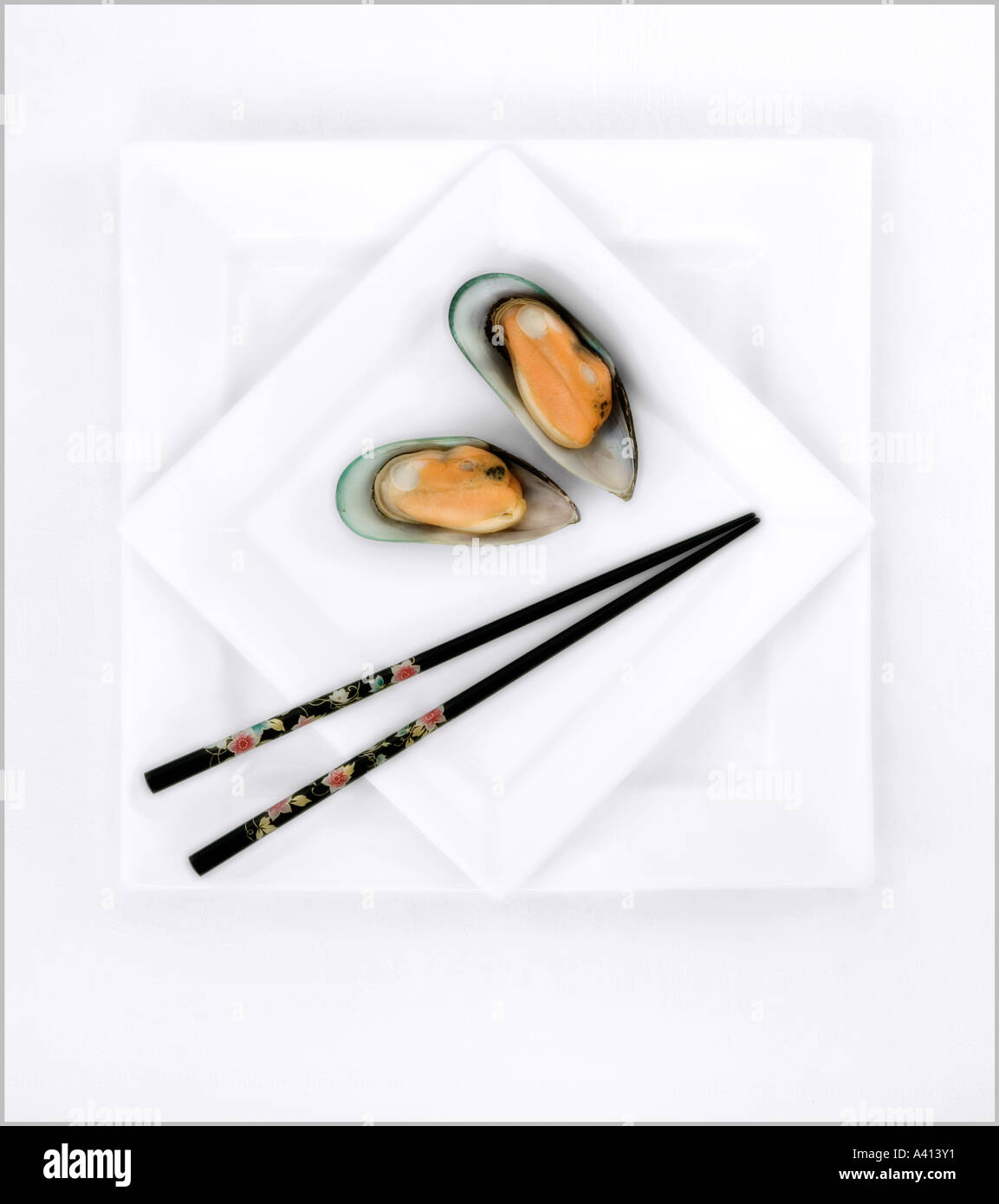 Pair of black chopsticks and two green shell mussels on two white plates at right angles Stock Photo