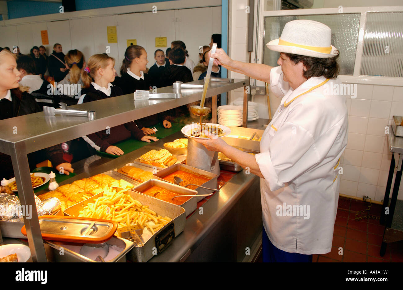 School pupils queue at hot counter waiting to be served by kitchen staff in school refectory UK Stock Photo