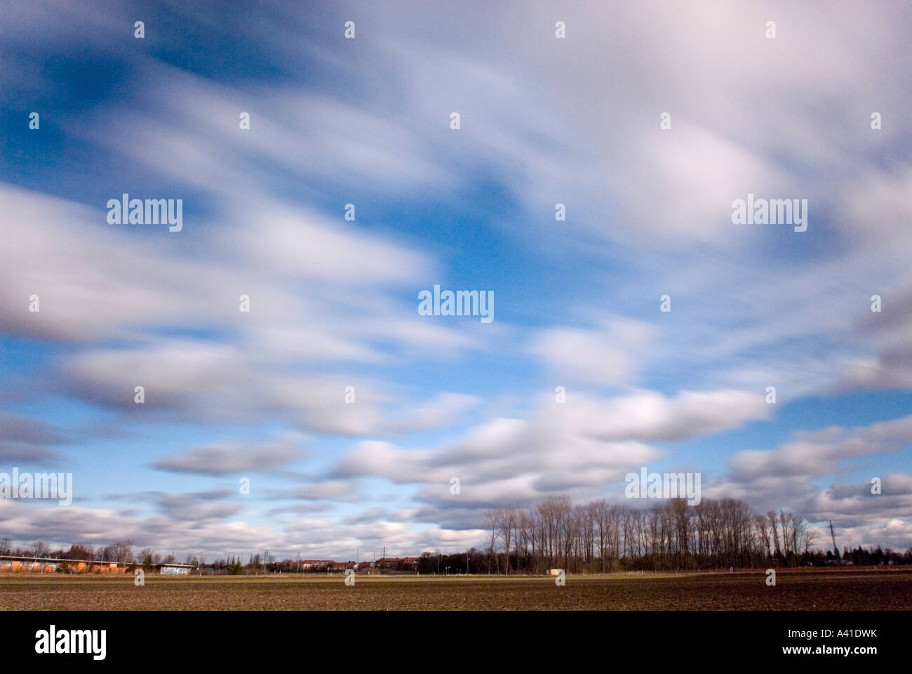 wintry landscape with field and bleak small wood and white clouds blurred while drifting near Munich Bavaria Germany Stock Photo