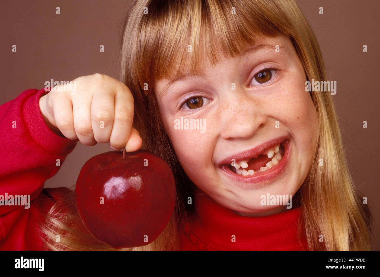 Little girl holding apple missing front teeth Stock Photo