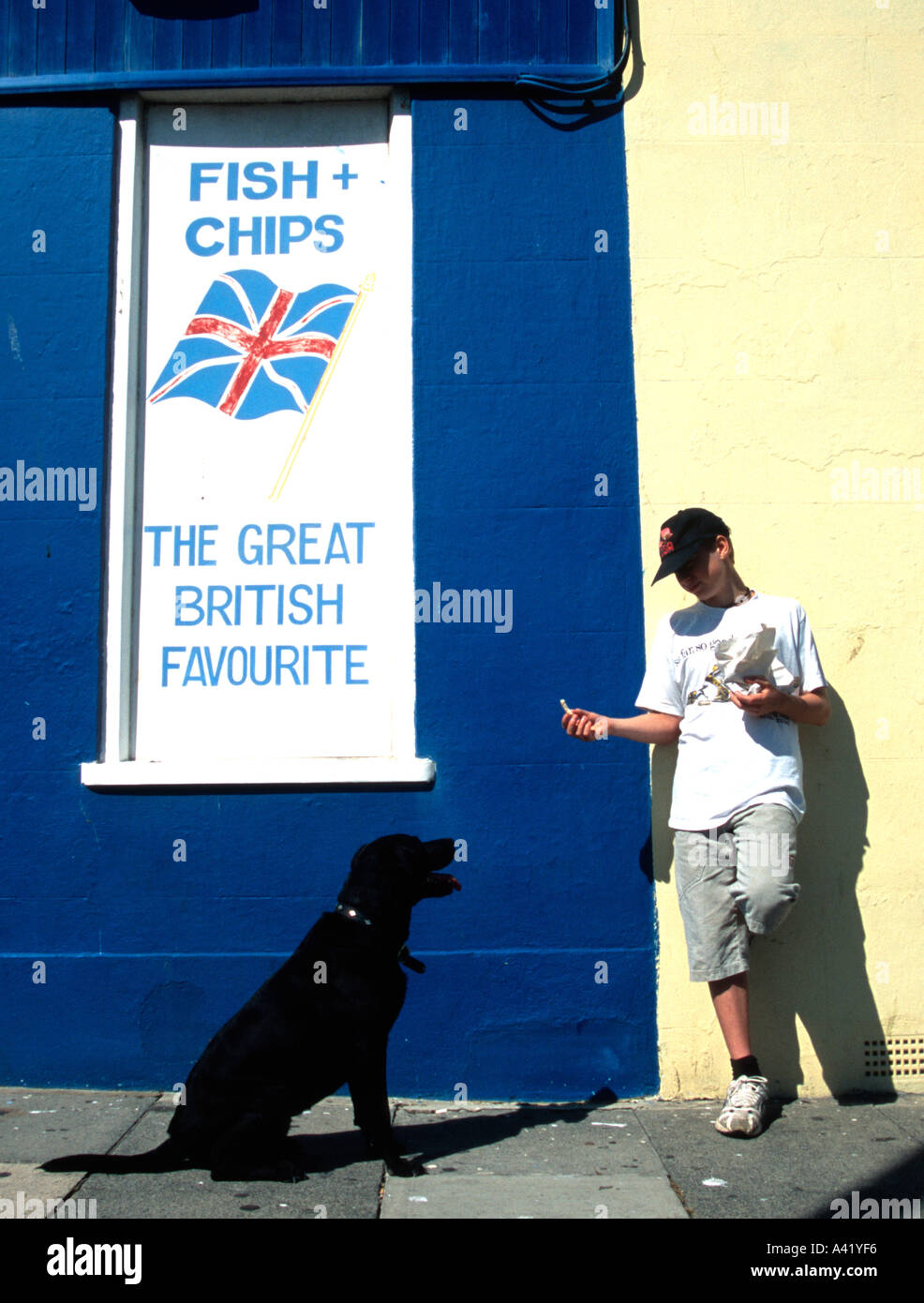 Boy throwing chip for jumping dog Fish Chip shop Fish and Chips Hastings East Sussex England Britain Europe EU Luke Hanna Iggy Stock Photo