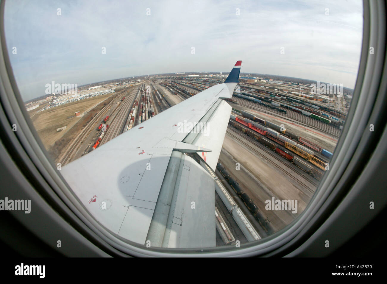 View out of an airplane window of a train yard and the plane wing with the flaps down Stock Photo