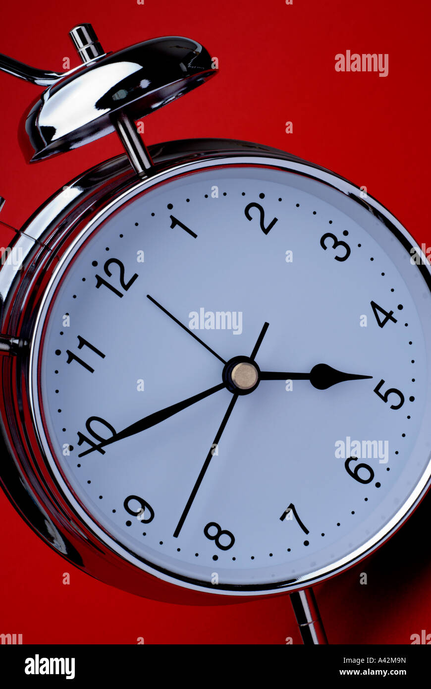 Clock at angle with silver alarm bell on red background Stock Photo