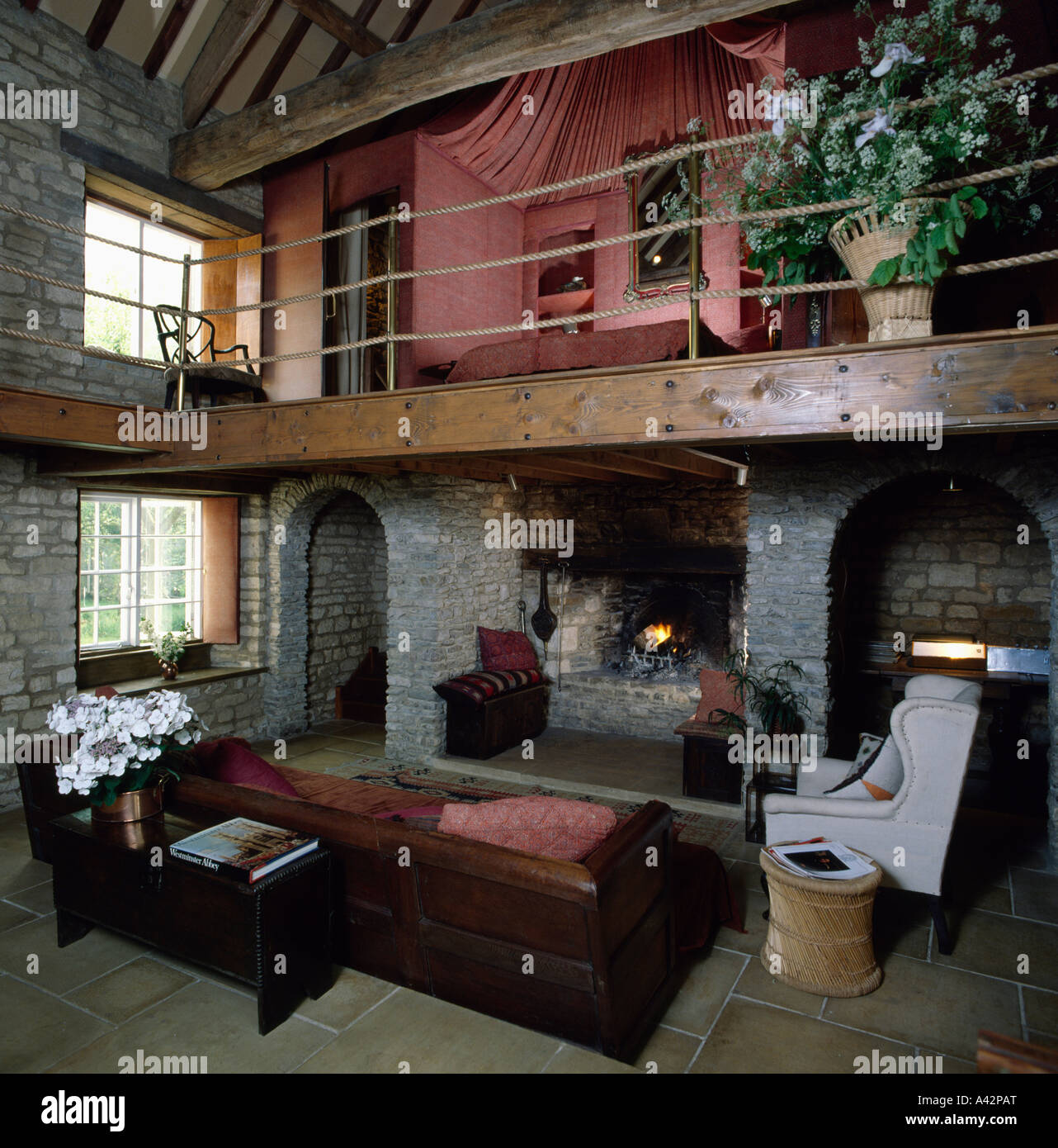 Double-height living room with mezzanine gallery tented bedroom and large  wooden sofa with pink cushions Stock Photo - Alamy