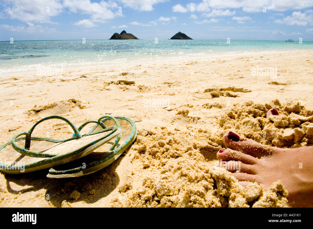 Toes in the sand near discarded flip flops on beach in Oahu Stock