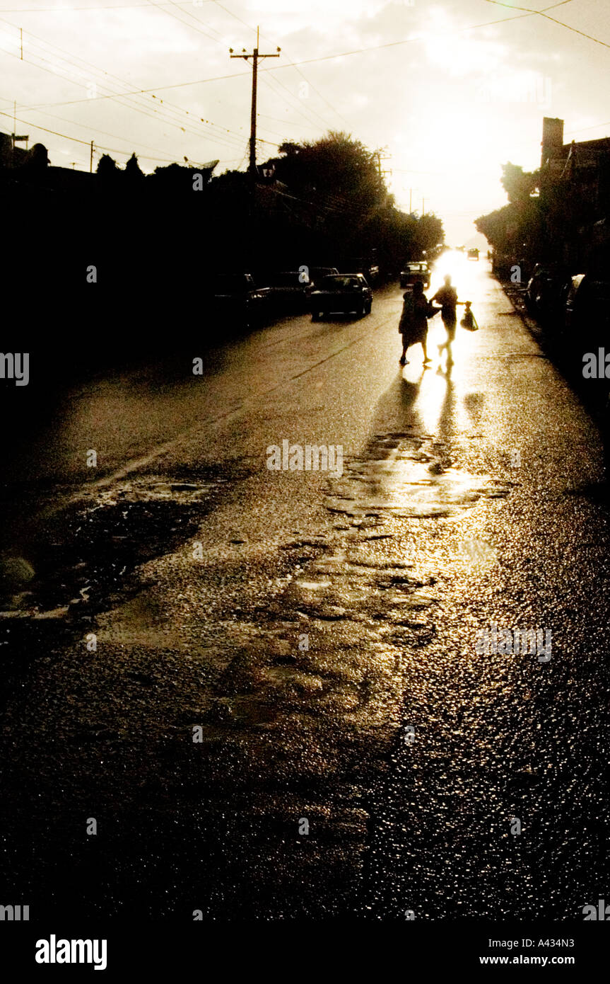 2 pedestrians silhouettes cross rain slicked highway in village near Lake Chapala in state of Jalisco Mexico Stock Photo