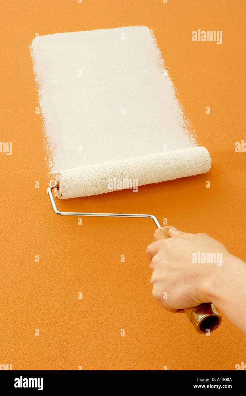 ROLLER APPLYING WHITE PAINT TO YELLOW WALL Stock Photo