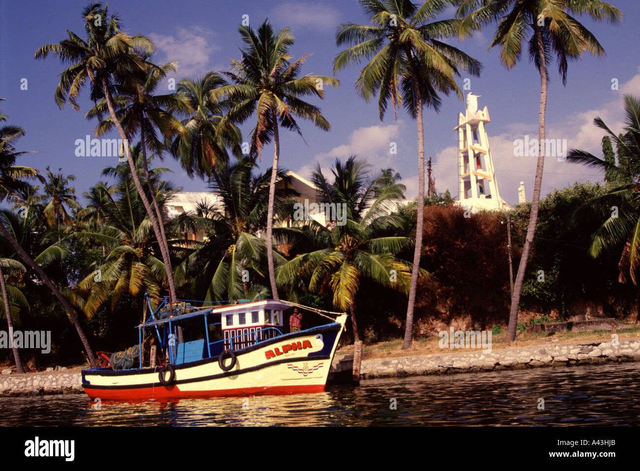 A wooden boat moored in a palm fringed canal with a bell tower of a