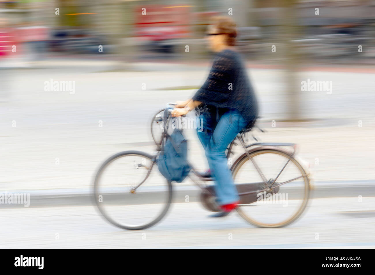 Blurred female cyclist riding at speed in the centre of Amsterdam, dressed in jeans and a dark-coloured top Stock Photo