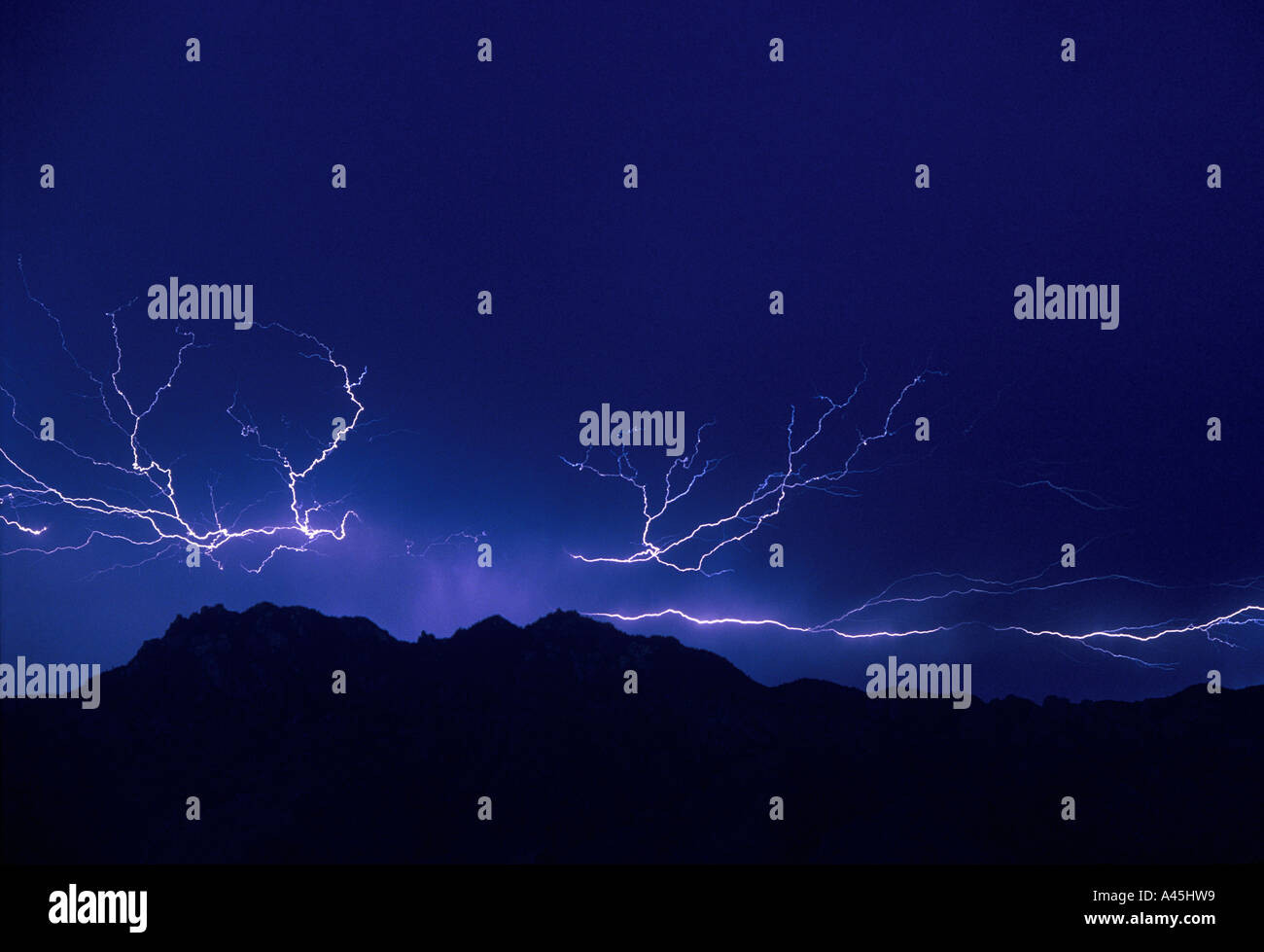 Lightning  strikes against a dark blue sky over the silhouette of mountains in Southern Arizona USA. Stock Photo