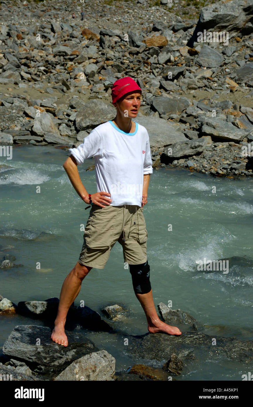 Young woman stands lofty and barefoot in icecold water of Glacier de Bionnassay Haute-Savoie France Stock Photo
