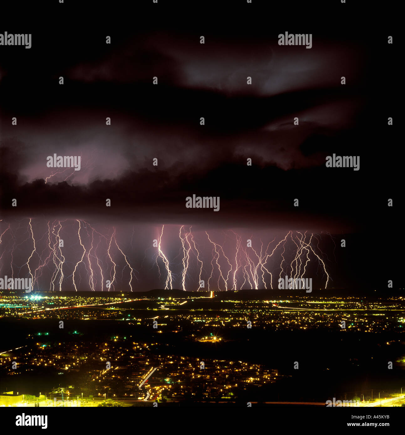 Lightning  bolts strike from a dark and stormy sky over the glowing cityscape of Tucson Arizona. USA Stock Photo