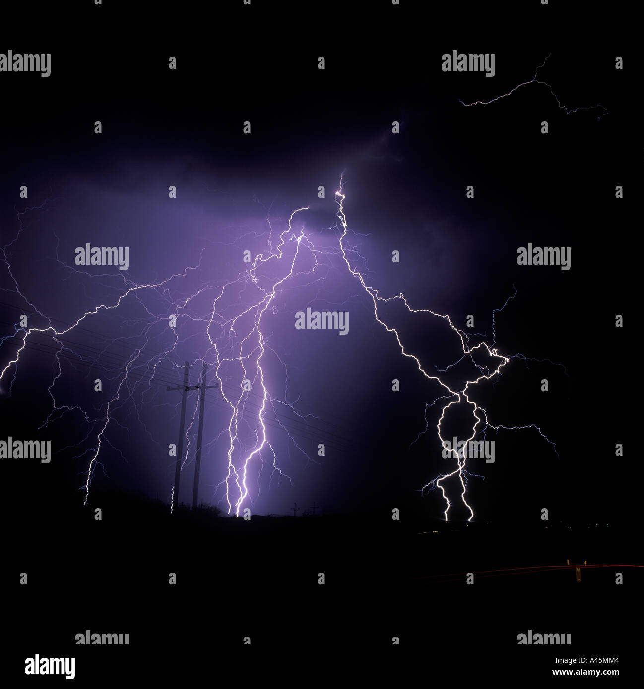 Lightning strikes from the sky with powerlines silhouetted in the foreground over Southern Arizona, USA. Stock Photo