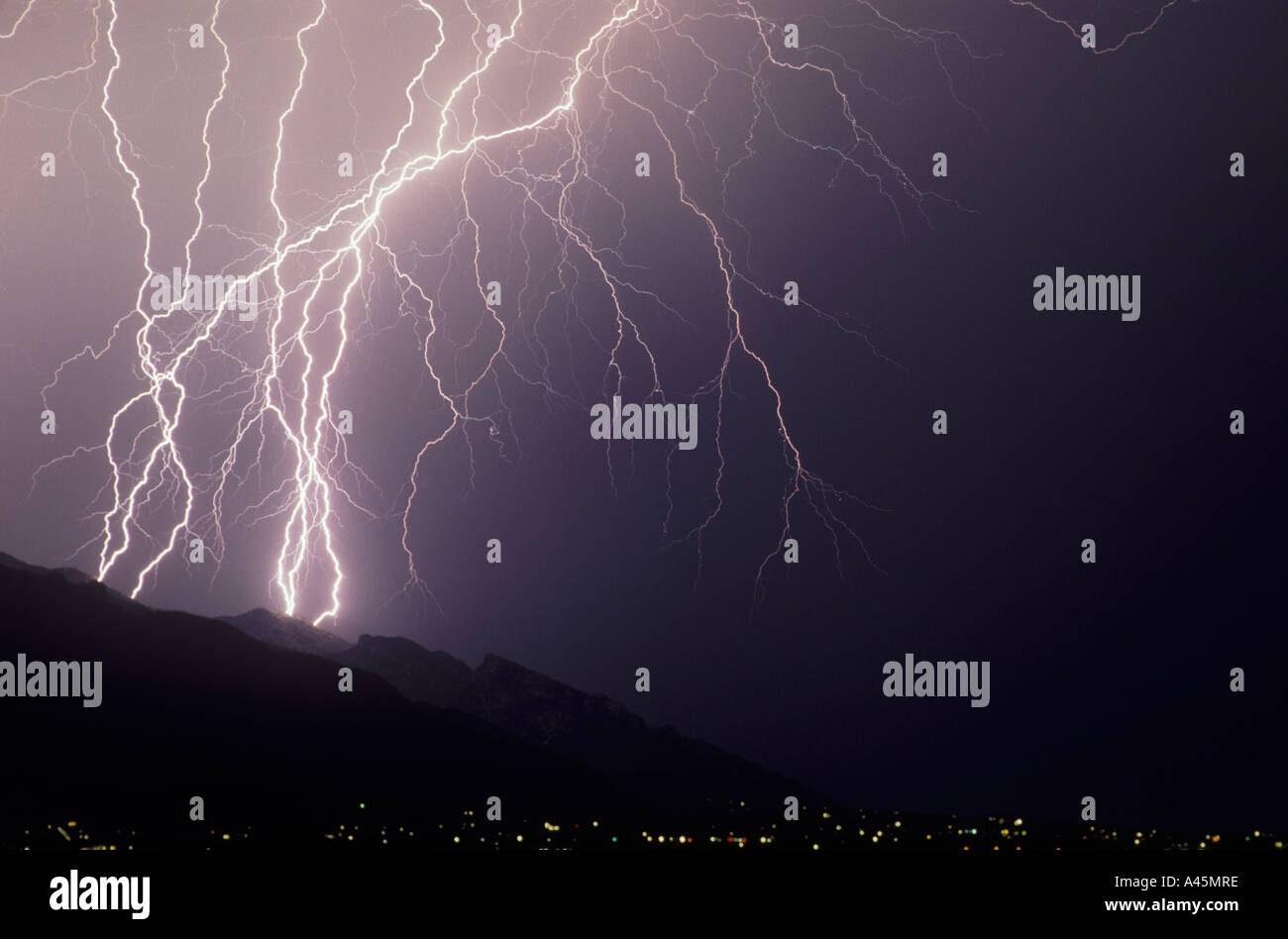 Bolts of lightning strikefrom a stormy sky over a mountain range and city lights in Southern Arizona, USA. Stock Photo