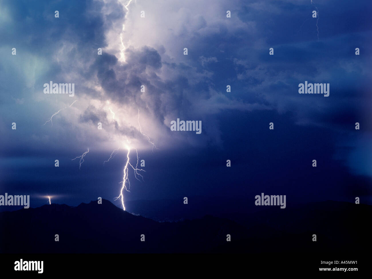 Lightning  strikes against a stormy dark blue sky over the silhouette of mountains in Southern Arizona USA. Stock Photo