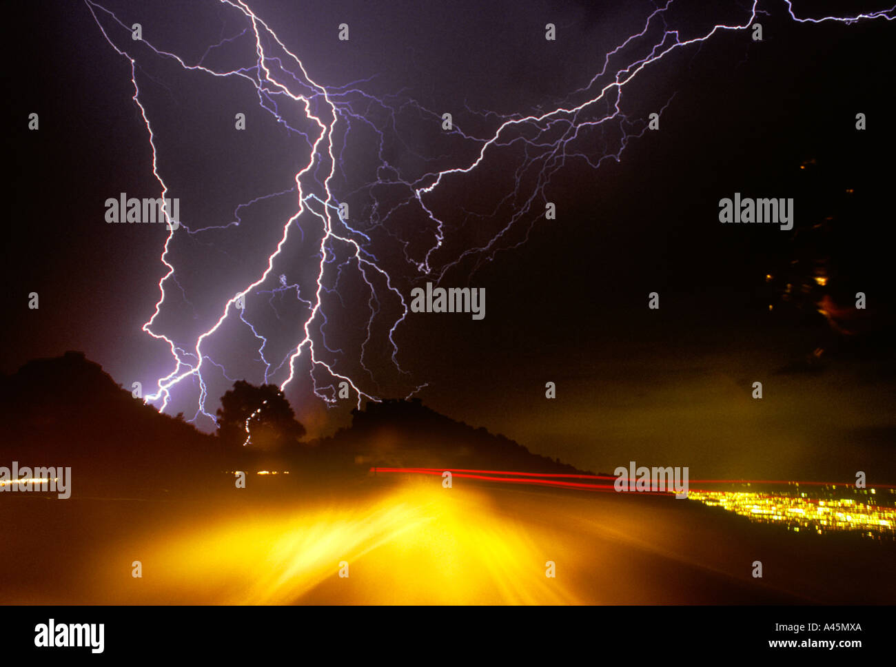 Lightning bolts strike down from a stormy sky with blurred traffic lights in the foreground in Southern, AZ. USA. Stock Photo