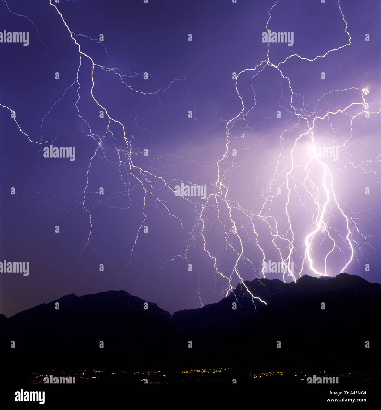 Lightning bolts strike from a purples sky with a mountain range silhouette in the foreground in Tucson, AZ, USA. Stock Photo