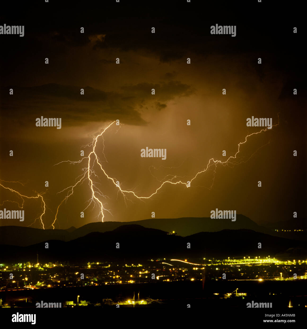 Lightning  bolts strike from a dark and stormy sky over the glowing cityscape of Tucson Arizona. USA Stock Photo