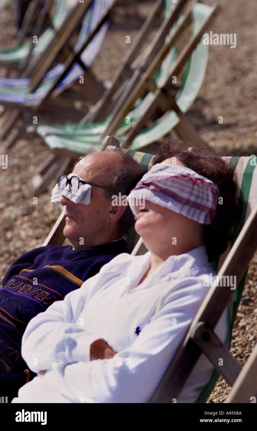 an elderly couple sit on deckchairs on brighton beach on the south coast of england Stock Photo