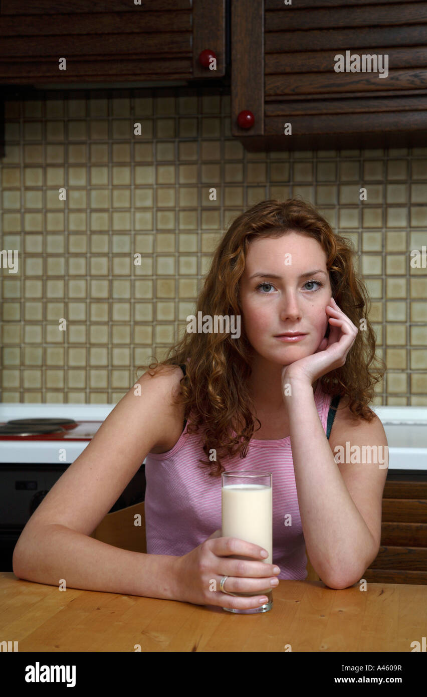 Young woman sitting at a kitchen table with a glass of milk Stock Photo