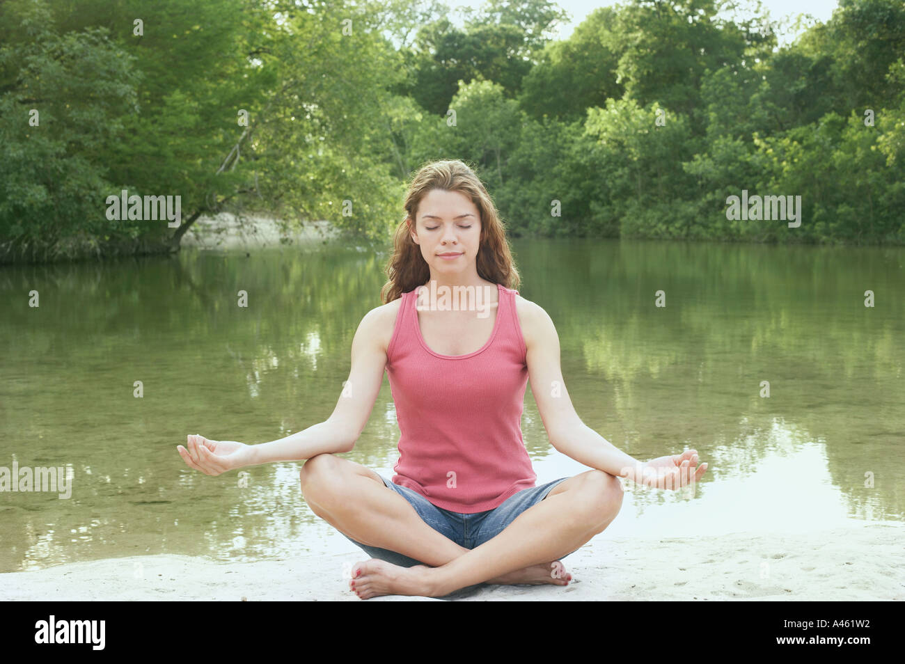 Woman in lotus position beside water Stock Photo