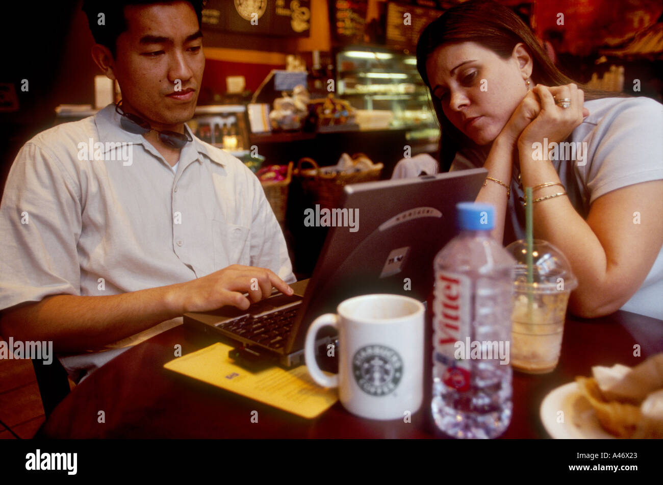 john and shane vu browse the internet with a laptop in a starbuck s cafe on old broad street in the city of london uk Stock Photo