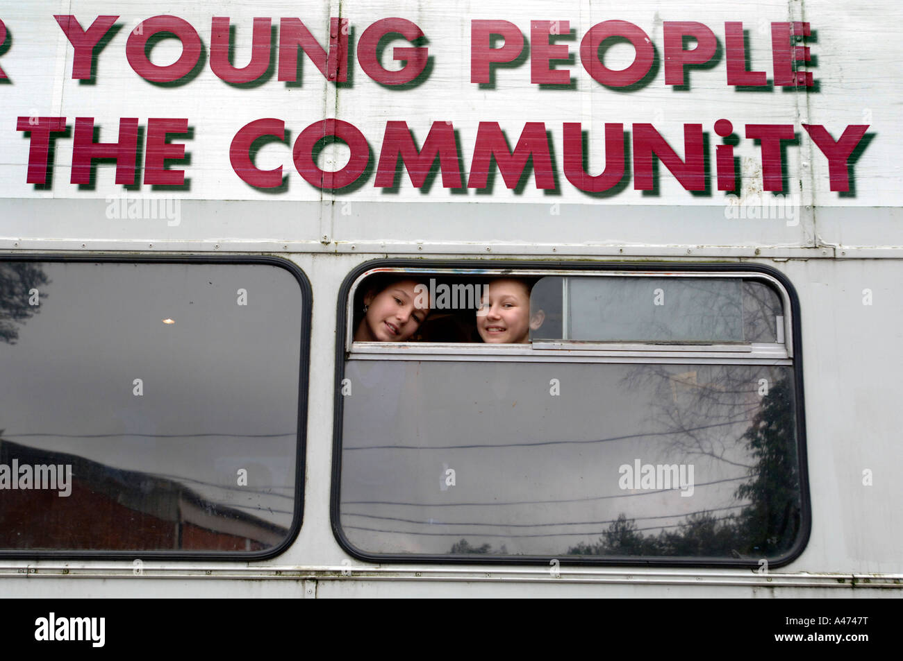 Two cheeky smiling girls look out of the window of a community bus Stock Photo