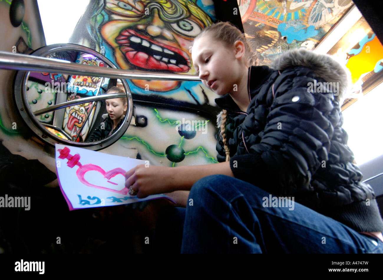 A young girl is reflected in a mirror as she sits on graffiti covered metal stairs and gazes at a heart. Stock Photo