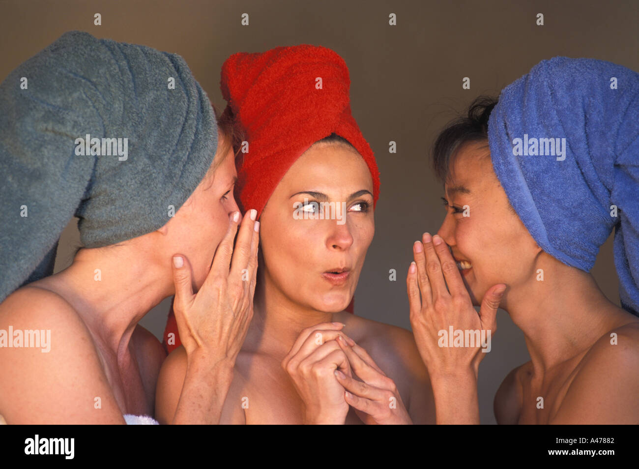 Three women of ethnic mix with colorful bath towels sharing gossip Stock Photo