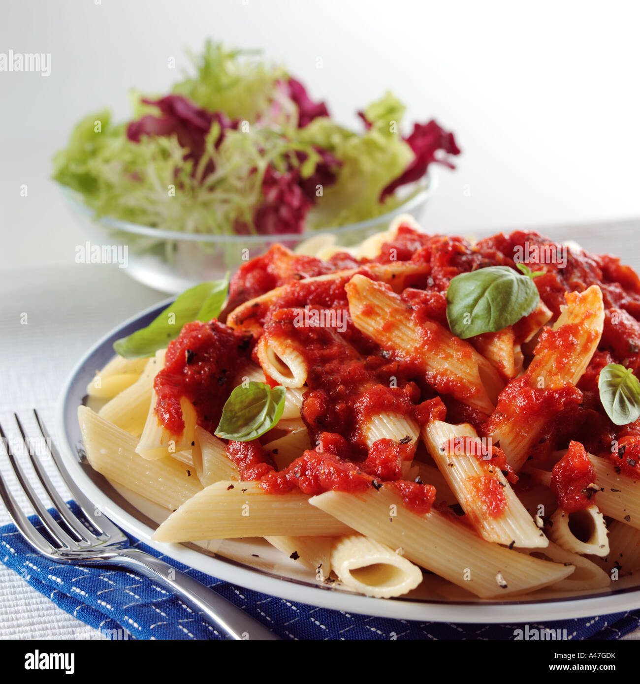 A plate of Italian penne napolitana with a bowl of salad behind on a white background editorial food Stock Photo