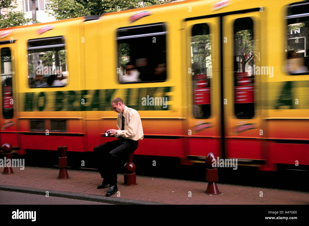 amsterdam tram travelling at speed passes behind a  passenger using a mobile  phone to send a text  message Stock Photo