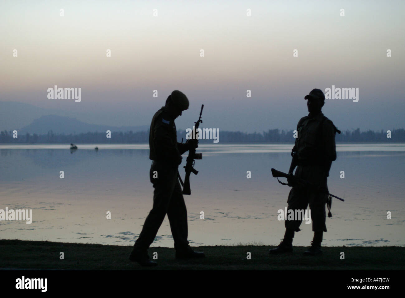 Two soldiers are silhouetted while carrying their weapons on the banks of Dal Lake in Srinagar in Kashmir in India Stock Photo