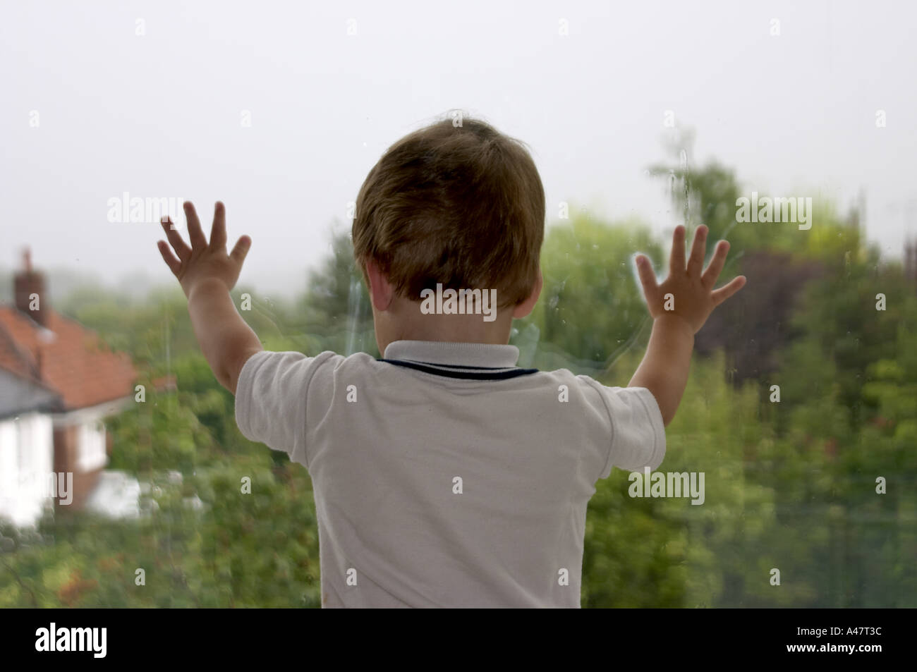 Young boy looking out of a window at a day of driving rain He can t go ...