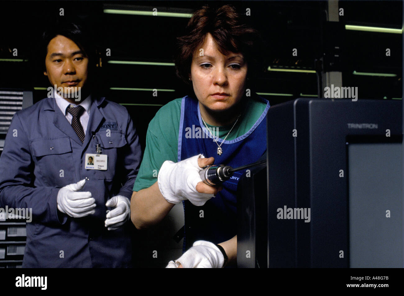 Japanese manager supervising a woman at The Sony factory assembling a Trinitron television using an electric screwdriver Stock Photo