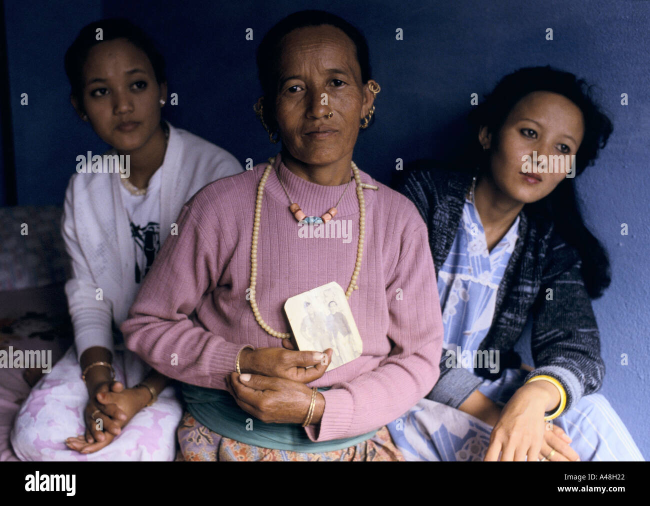 A widow of a gurkha soldier holds his picture with her daughters beside her. His death put them into a life of poverty Stock Photo