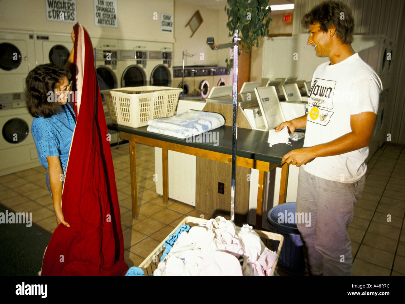 A woman talking to a man while folding up her red duvet in a launderette in Clinton Iowa Stock Photo